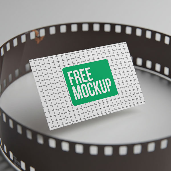 Film Strip Business card Free Mockup. A grid-patterned business card with the words "Free Mockup" is placed inside a curled strip of photographic film against a plain background.